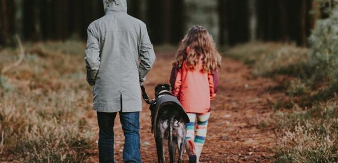 Adult, child and greyhound walk through the woods